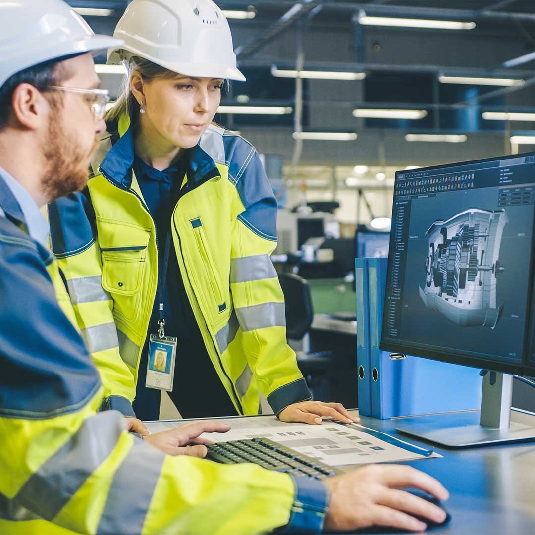 A person and person wearing hard hats looking at a computer screen