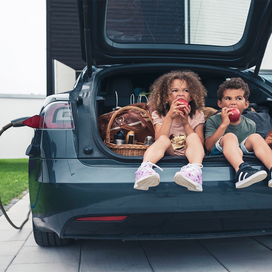 two kids eating apple sitting at the car trunk