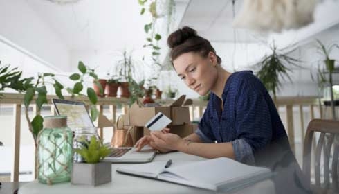 Female plant shop owner with credit card paying bills online at laptop in workshop