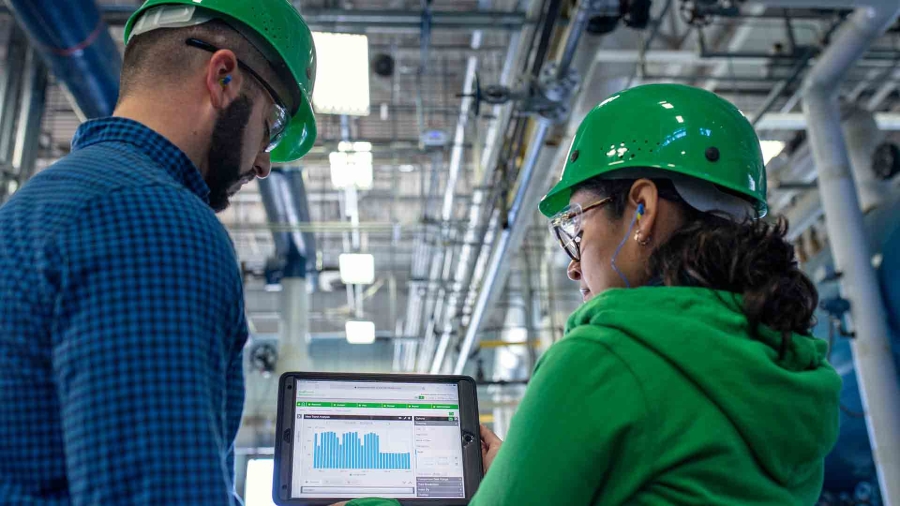 A male and a female employee wearing protective hat and discussing inside a smart factory