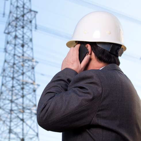 Executivo usando um celular ao lado de uma torre de distribuição elétrica.