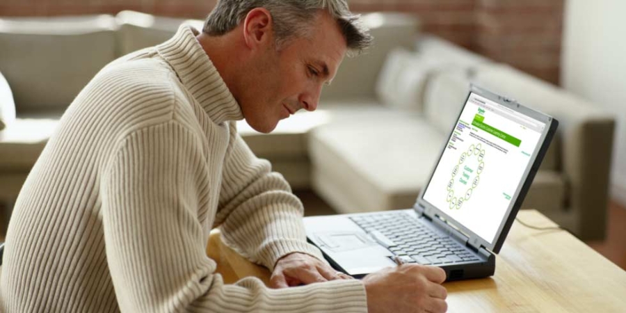 Male writing down notes by the computer.