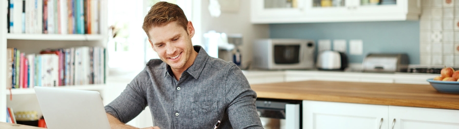 Shot of a young man using a laptop and writing notes at home