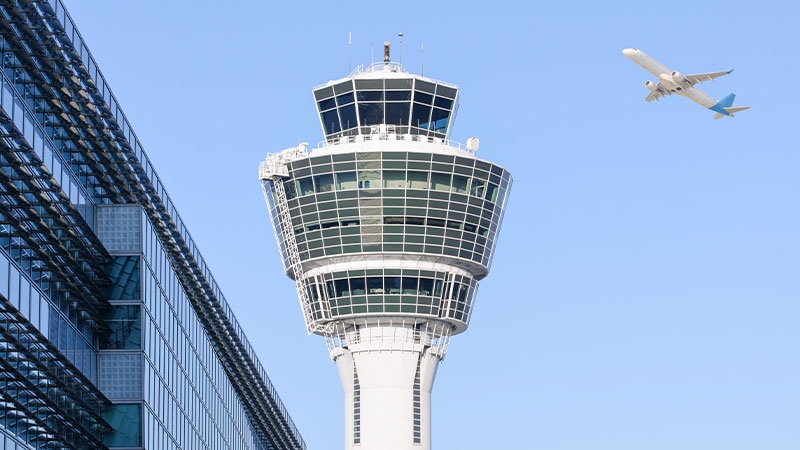 An airport control tower overseeing a departing airplane as it takes off from the runway.