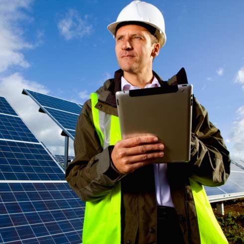 Ingenieur mit digitalem Tablet steht vor Solarmodulen, Energiemanagement.