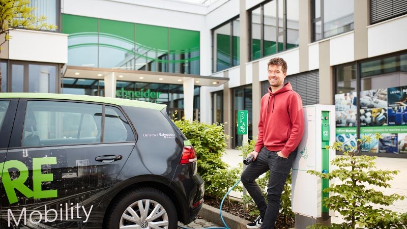 Dual studies, student next to an electric car and an e-charging station