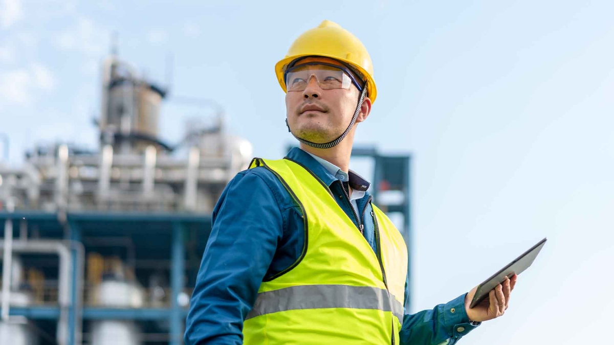 A person in a yellow hard hat and safety vest holding a tablet