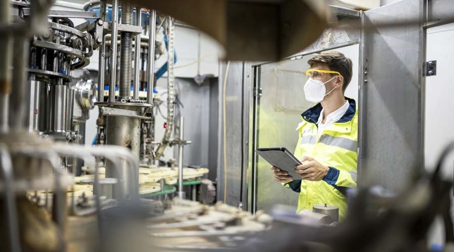 A male employee with a digital tablet in hand inspecting a machinery in factory