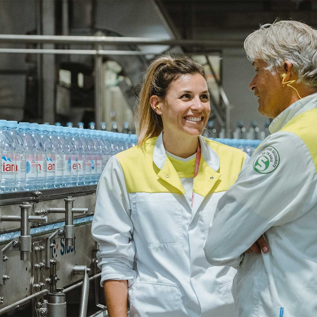 A person and person in white coats standing next to bottles of water