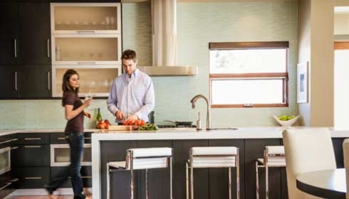 hombre en la cocina cortando vegetales mientras una mujer lo mira, en su casa con eficiencia energética