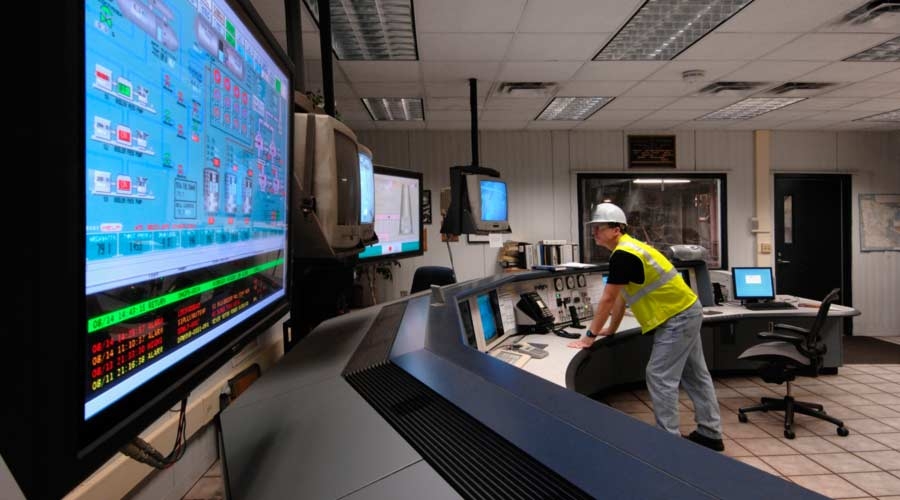 Technician in hard hat monitoring computer screens in control room, facility management software.