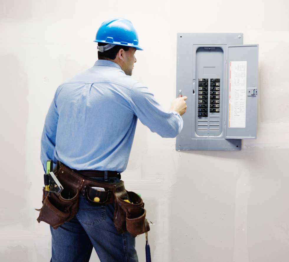 Male electrician making adjustment to fuse box rear view