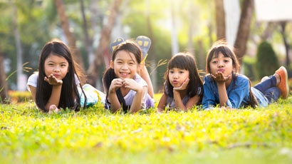 Malé asijské dívky leží na zelené trávě pod slunečním světlem