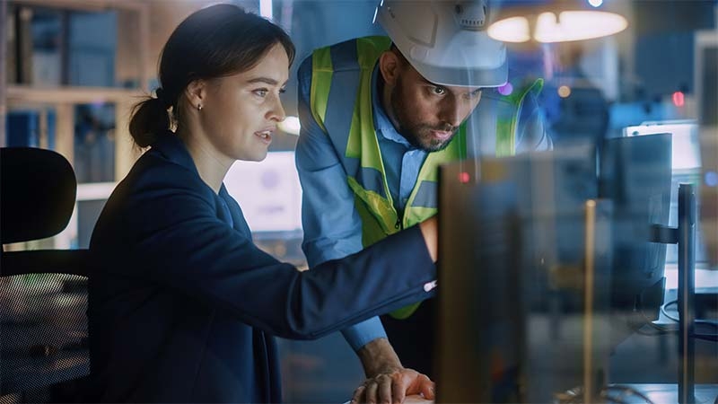 A person and person in hardhats looking at a computer screen