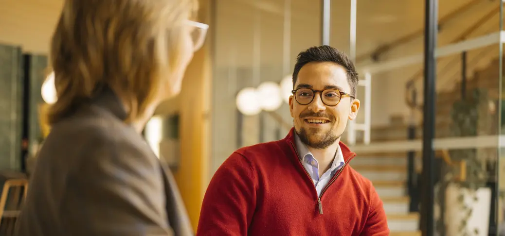 Deux personnes dont l’une portant un pull rouge et des lunettes, assises côte à côte