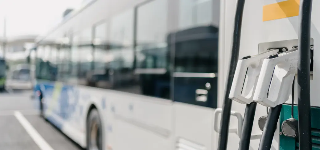 A white electric bus is connected to a charging station, zoomed in on the cables and connectors.