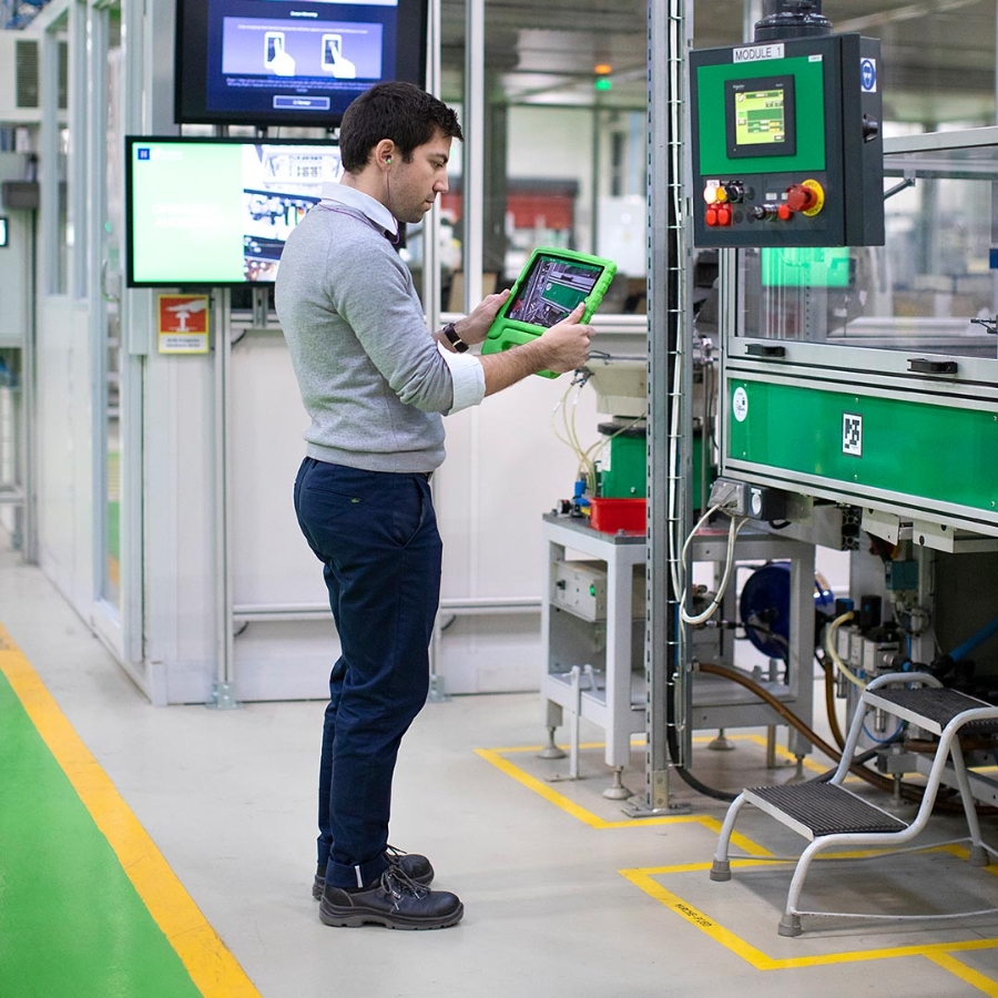 A male employee inside a factory is scanning the QR code of a machine by his digital tablet