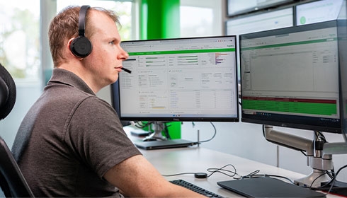 A person wearing headphones sitting at a desk with two computer monitors