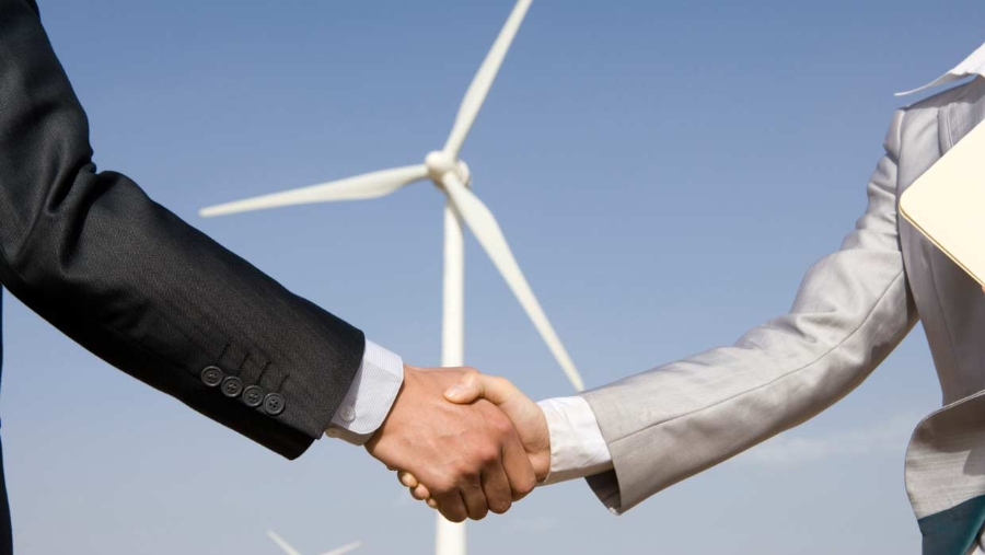 Two men shaking hands in front of a wind turbine