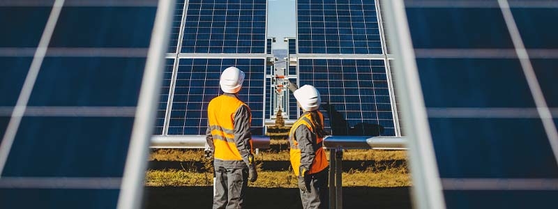 Two men in safety vests standing in front of solar panels