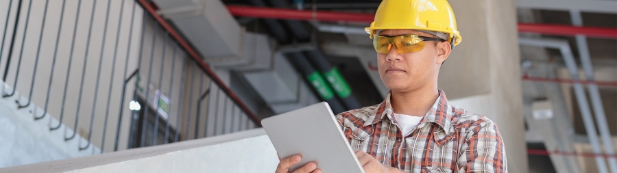 a construction worker with yellow helmet and glasses using a tablet