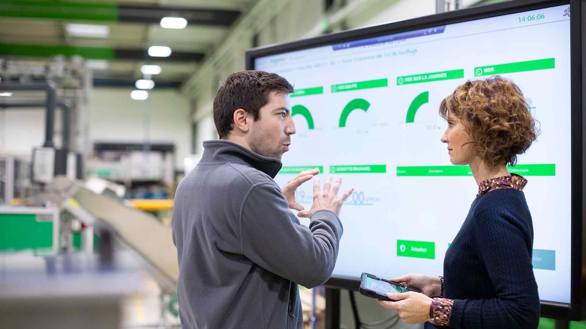 A female employee with a digital tablet in hand inside a factory discussing with a male employee