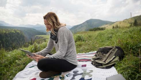 Woman using digital tablet on blanket in remote rural field