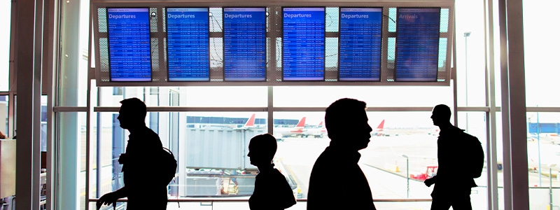 Passengers walking through airport lobby with flight information board in background