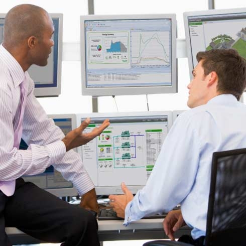 Business men in front of monitors with Schneider Electric monitoring software, reviewing sustainability reporting, big data analytics.