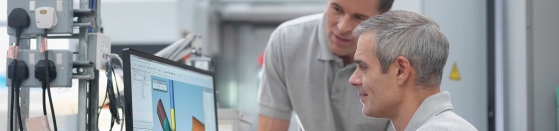 Engineers watching CNC lathe progress on screen in orthopaedic factory