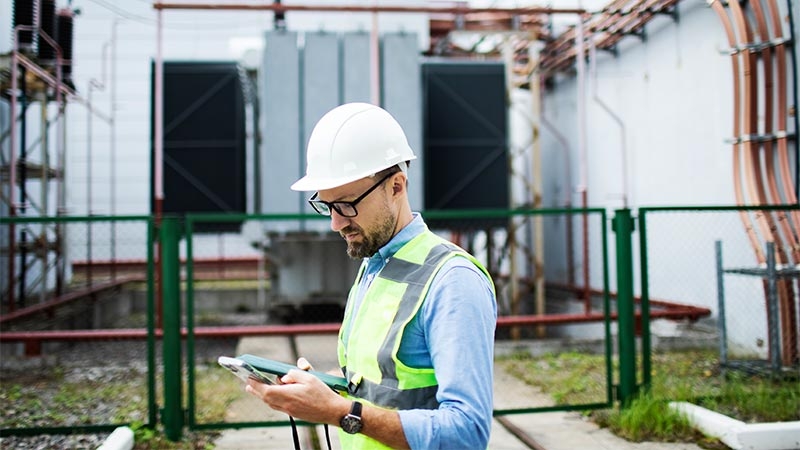 A person in a safety vest and hard hat looking at a tablet