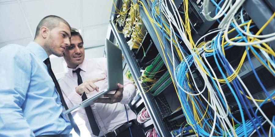 Two men looking at a laptop computer in a network data centre, energy management software, energy efficiency.