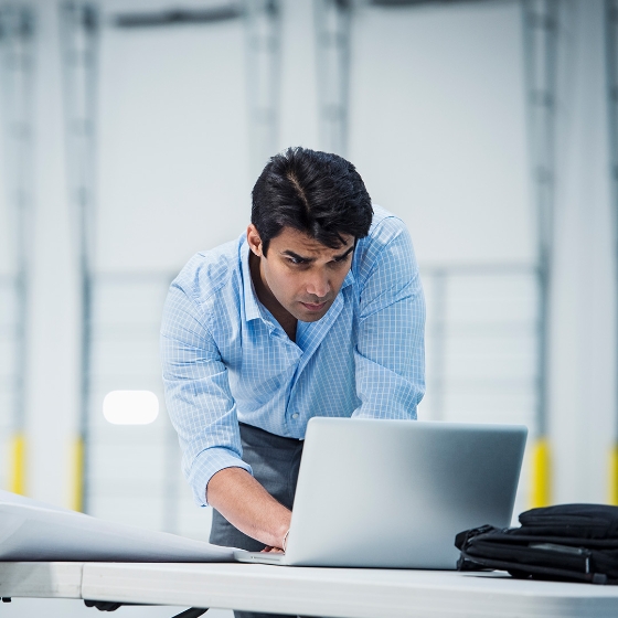Male employee standing and working on his laptop in office