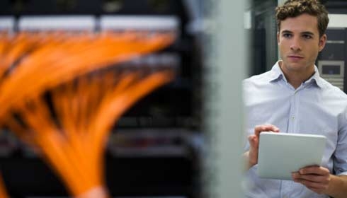 Computer technician using digital tablet performing maintenance check of mainframe equipment