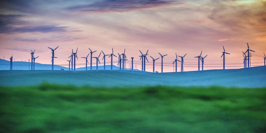 Distant View Of Wind Turbines On Farm At Sunset