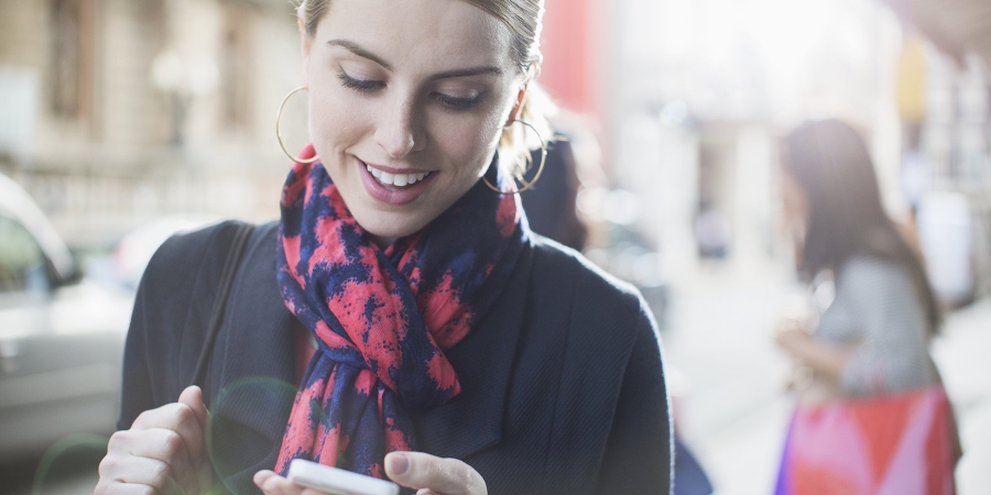 young lady wearing scarf smiling while looking at her mobile phone