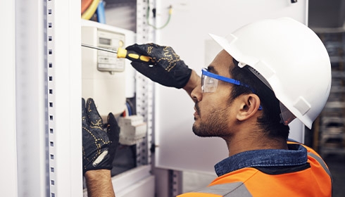 A person wearing a hard hat and gloves working on a electrical box