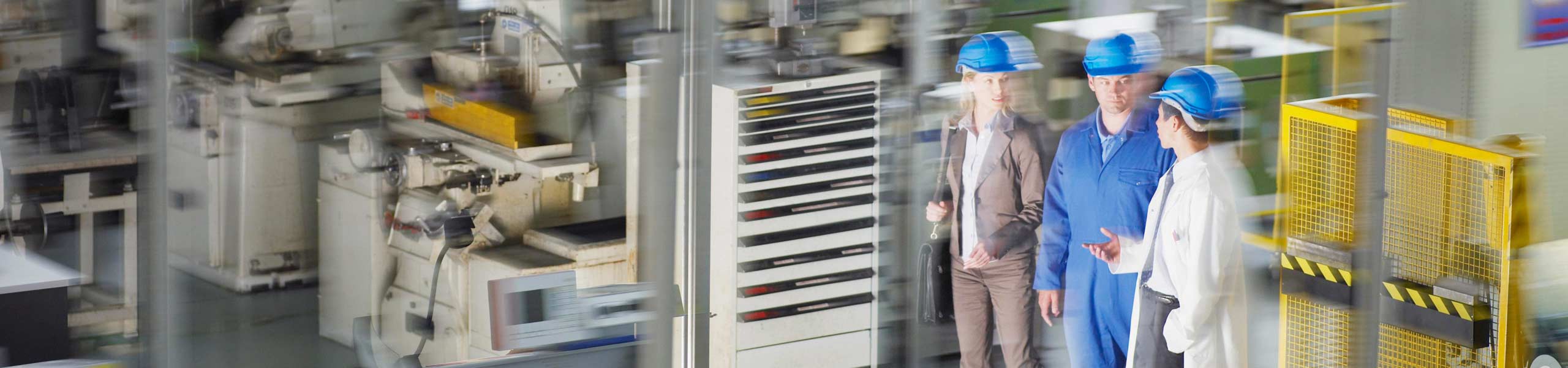 Business people in hard-hats walking on factory floor with lots of machines, power management, plant solutions.