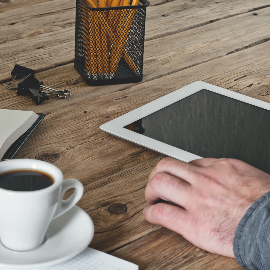 Closeup shot of a coffee cup and a digital tablet placed on a wooden desk