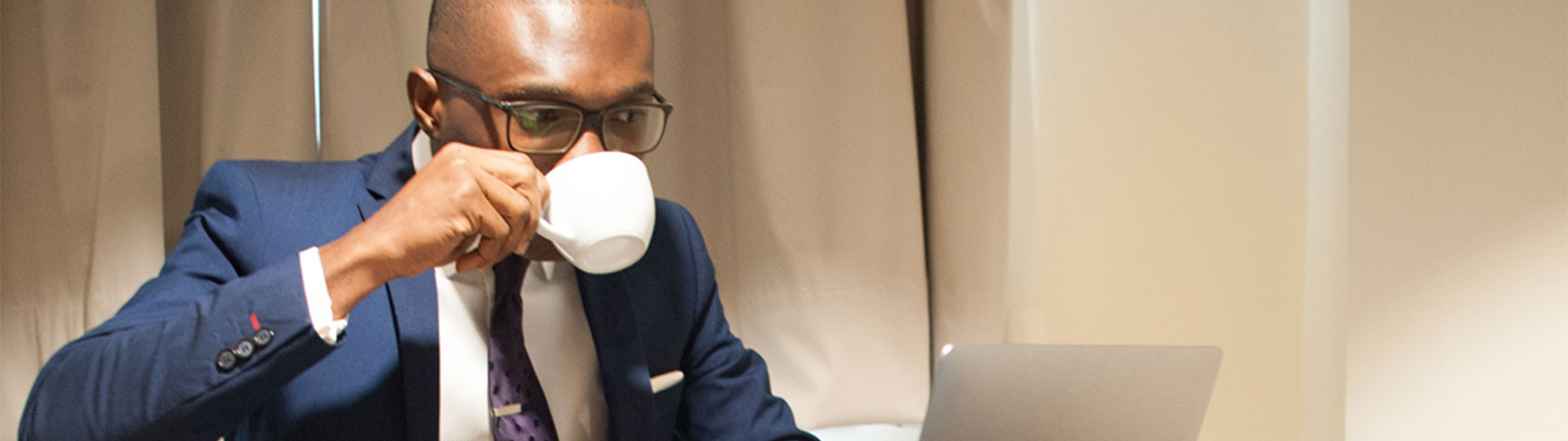 Man wearing a suit and working on a laptop drinks coffee