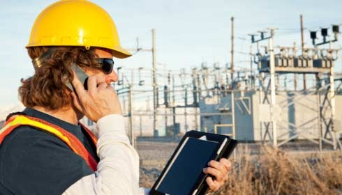 Power line technician using phone and tablet, sustainability reporting, Internet of Things.