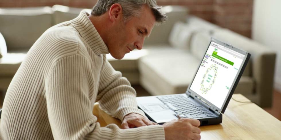 Bildet viser en mann som tar notater ved datamaskinen.