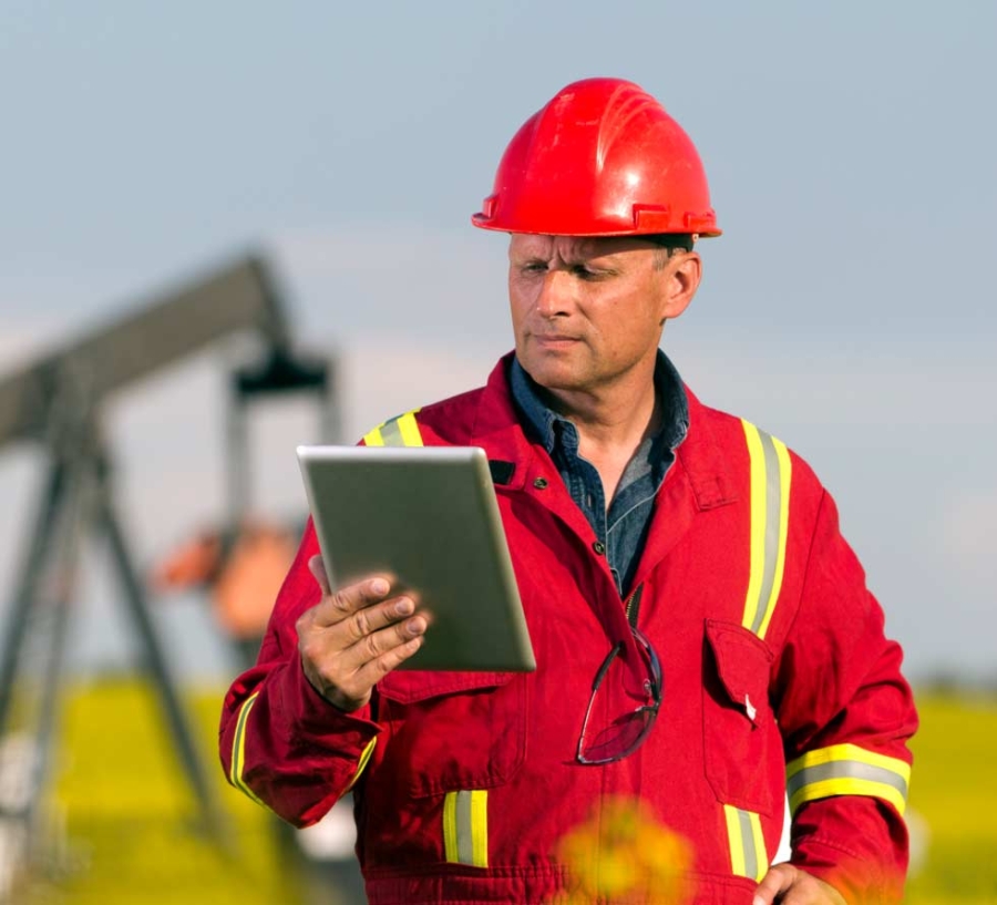 Worker with tablet computer in front of oil rig, oil and gas, sustainability reporting, Internet of Things.