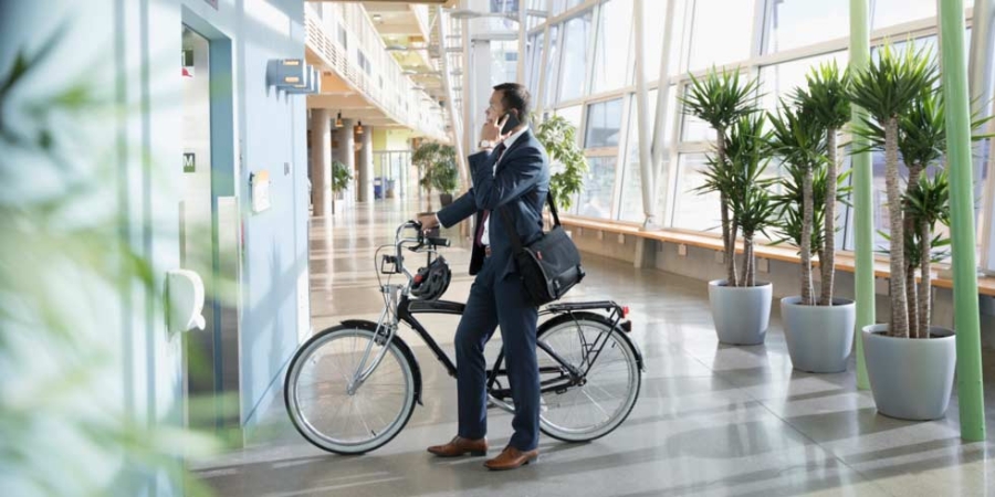Businessman commuter with bicycle talking on smart phone, waiting at elevator in office lobby