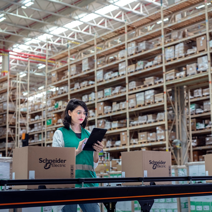 A female employee holding a digital tablet and inspecting the products moving on the conveyor belt in a smart logistic center