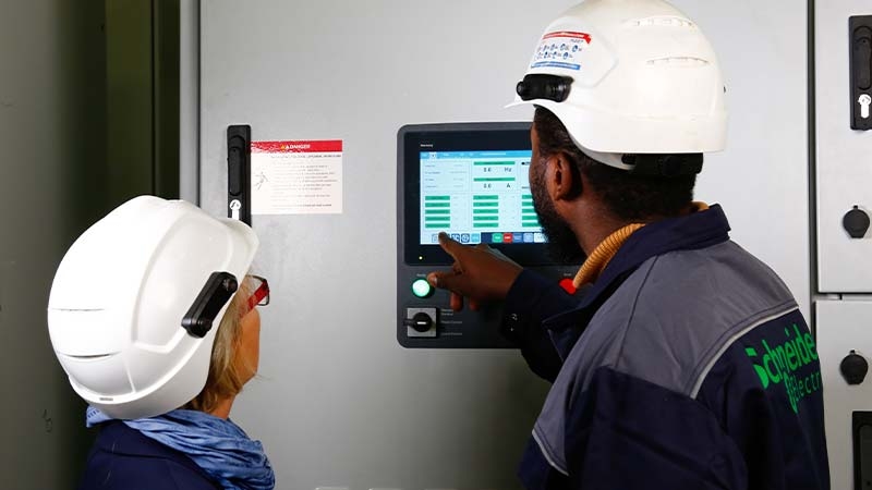 A person and person wearing hardhats looking at a machine