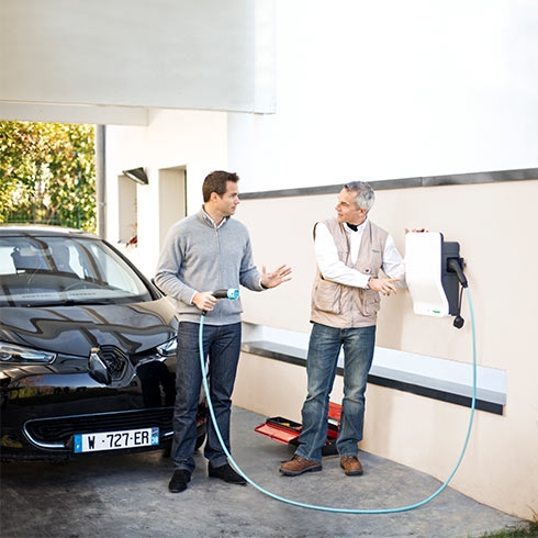Two men standing by a car, discussing Evlink charging station which is wallmounted.