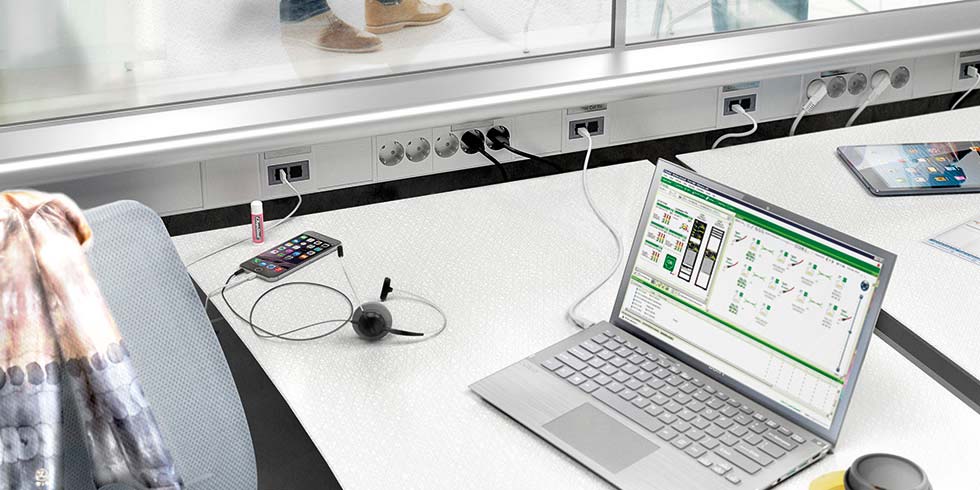 Skrivbord med laptop kopplad till installationssystem, fönsterbänkskanal