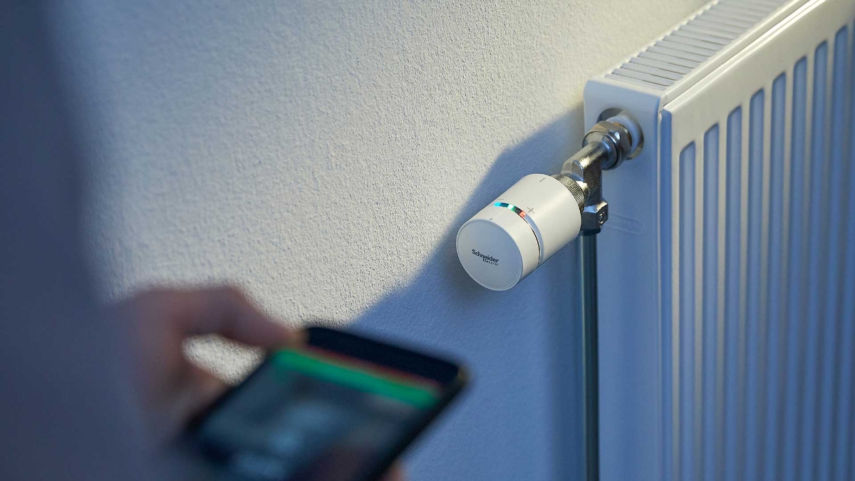 Wiser radiator thermostat mounted on element, hand with mobile adjusting settings.