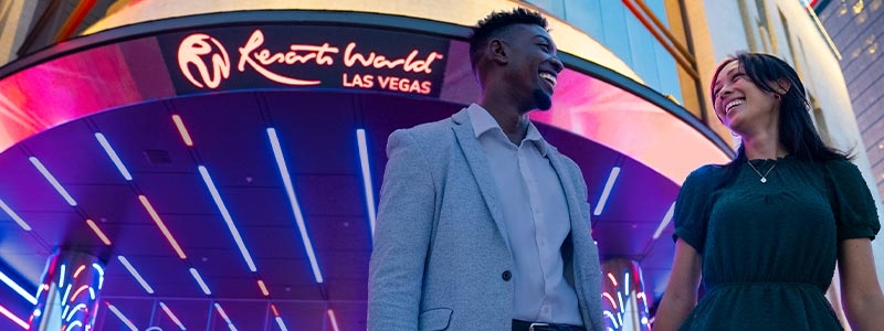 A person in a suit standing in front of a neon sign